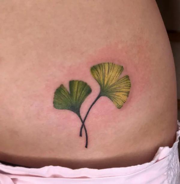 Two green ginkgo leaf low back tattoo