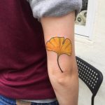 Yellow ginkgo leaf tattoo above elbow