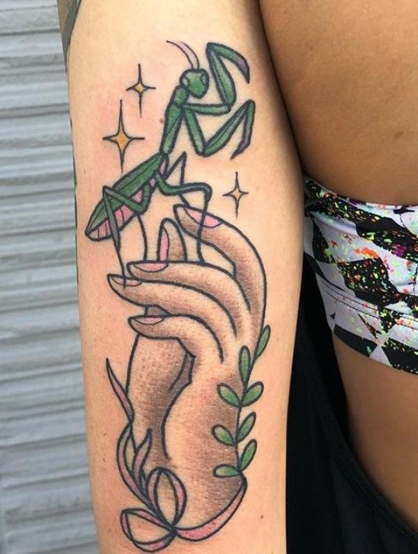 A hand holding a praying mantis with stars tattoo