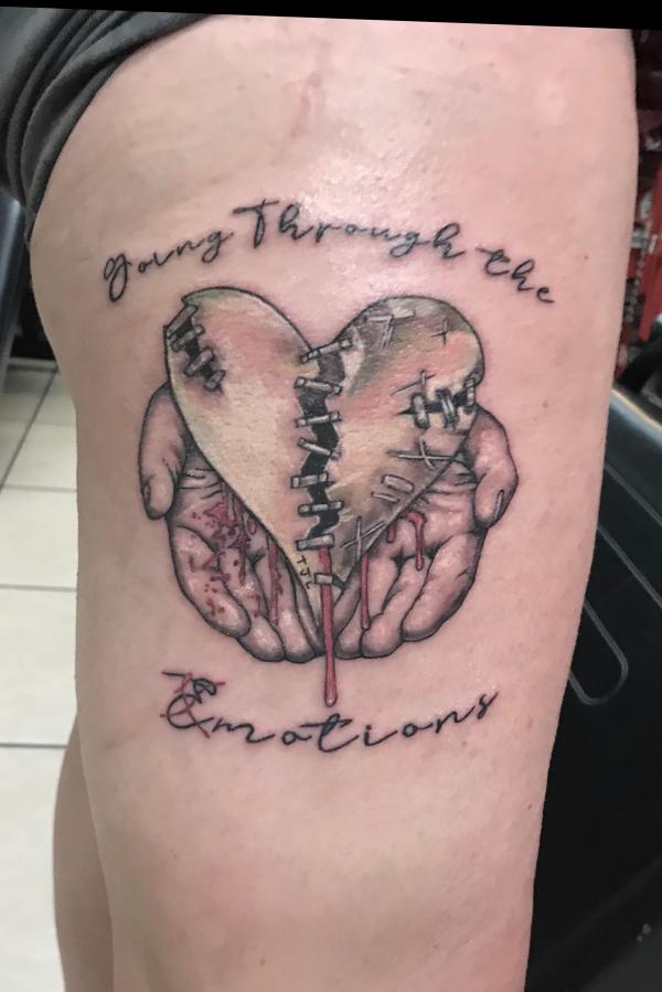Hands holding stitched broken heart tattoo with words going through emotions