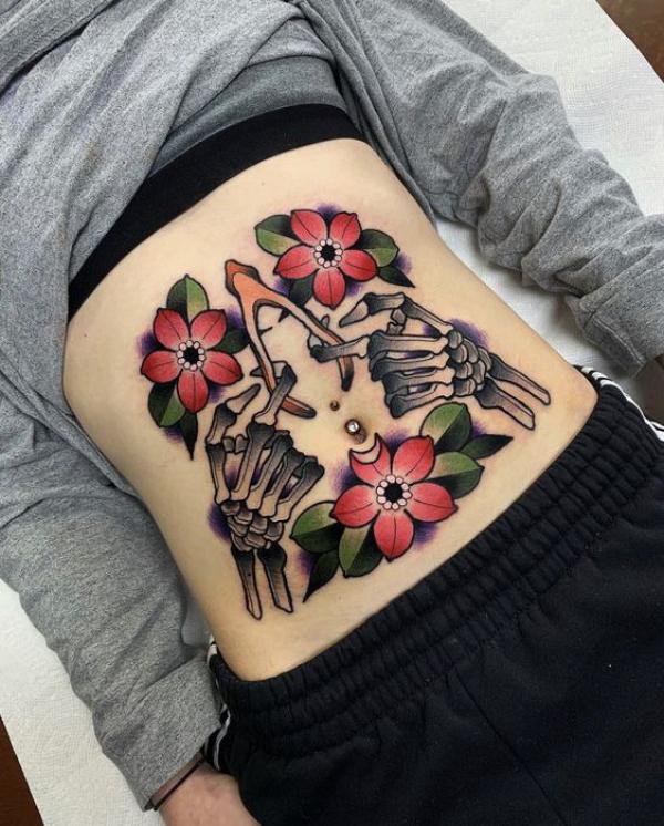 Traditional flowers and skeleton hand stomach tattoo