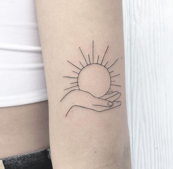 A hand holding the sun outline tattoo