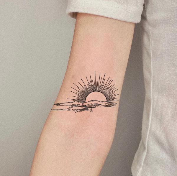 Rising sun and clouds tattoo above inner elbow