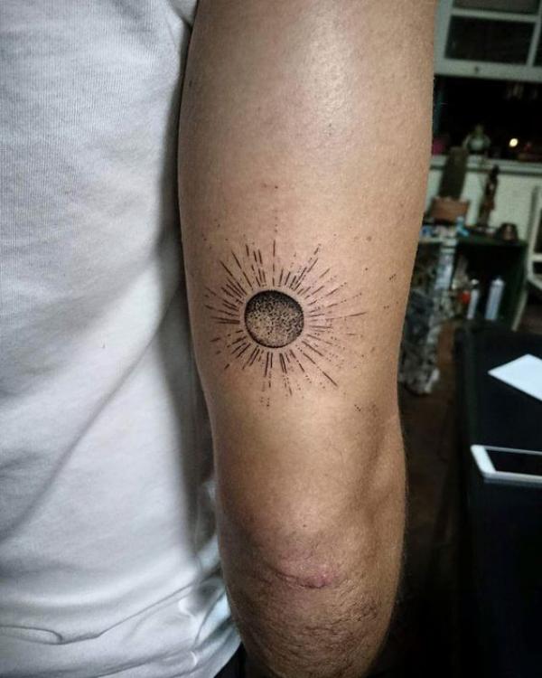 Small sun tattoo above elbow