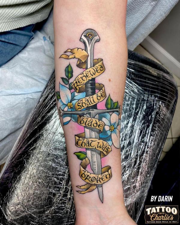Lord of the Rings sword with ribbon and flowers tattoo forearm