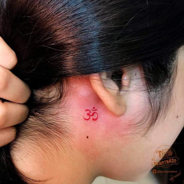 Red OM tattoo behind the ear